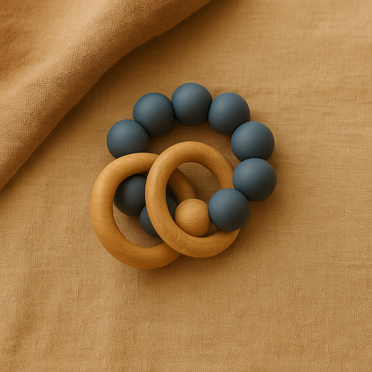 Blue silicone beaded baby teether with natural beechwood rings resting on a warm beige fabric.