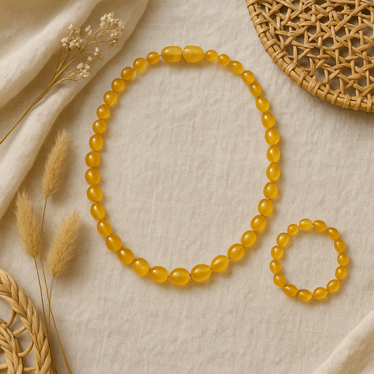 Boho-style honey amber baby teething necklace and matching bracelet set displayed on neutral linen with natural woven and dried floral accents.